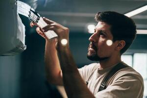 Man performs maintenance on air conditioning unit inside modern building during daylight photo