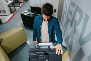Young man using a copier in a modern office space during the day photo