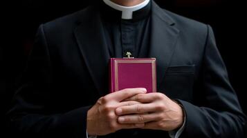 Clergyman holds a prayer book while dressed in formal black attire in a dimly lit setting photo