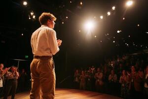 Actor performs on stage in a theater while audience applauds during a live performance at night photo