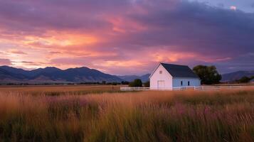 Sunset over a white barn in a colorful sky with mountains and fields in the foreground photo