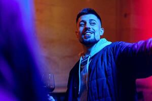 Young man enjoying social gathering while holding a drink with colorful lighting in background photo