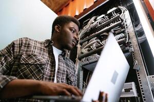 IT professional manages server rack while working on laptop in a data center during afternoon hours photo