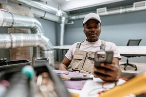 Skilled worker checking smartphone while seated in a modern workspace with exposed ductwork photo