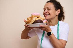 Smiling Woman Holding a Plate of Assorted Doughnuts While Wearing a Measuring Tape photo