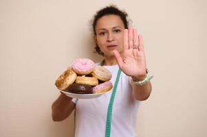 Woman Showing Rejection Gesture Over Plate of Doughnuts Emphasizing Healthy Choices photo