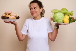 Balanced Choices. Woman Weighing Plates of Doughnuts and Fresh Vegetables photo