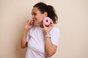 Woman Enjoying Pink Frosted Doughnuts While Smiling in a Fun and Playful Atmosphere photo