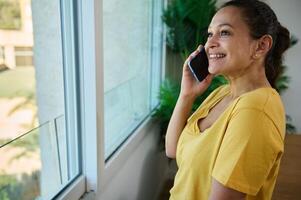 Smiling Woman Conversing on Mobile Phone While Enjoying the View from Her Home photo