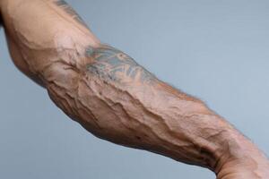 Muscular arm with prominent veins and intricate tattoo design on light background photo