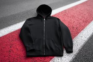 Black zip-up hoodie laid on a red and gray textured surface outdoors near a road photo