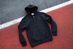 Black hoodie laid out on a red running track during daytime photo