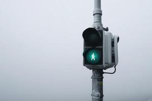 Green pedestrian signal shining in a foggy urban environment during early morning hours photo