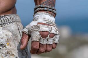 Athlete showing strong hand with worn gloves against coastal backdrop under clear sky photo