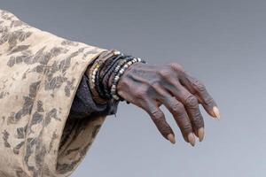 Elderly hand adorned with jewelry reaching out against a grey background photo