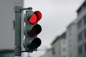 Red traffic light signaling vehicles to stop on a city street in overcast weather photo
