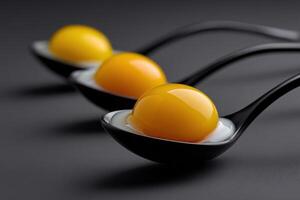 Three vibrant egg yolks resting in black spoons on a dark surface photo