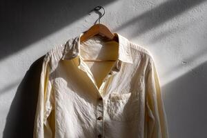 Sunlight highlights a light shirt hanging on a hook against a textured wall photo