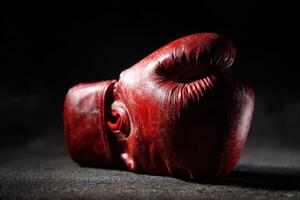 Red boxing glove resting on dark surface with shadows highlighting its worn appearance photo