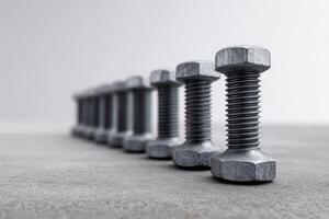 Row of steel bolts arranged with precision on a concrete surface in a workshop setting photo