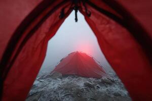 View from the inside of a red camping tent in misty mountain conditions at dawn photo
