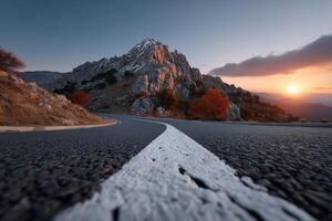 Road curves into an arrow pointing towards a vibrant sunset behind rocky mountains photo