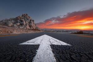 Road curves into a prominent arrow pointing toward a vibrant sunset photo