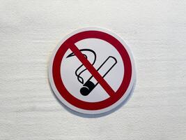 Close up of no smoking sign on white wall. Red circle with cigarette symbol and diagonal line emphasizes public health, safety and clean air in indoor environments photo