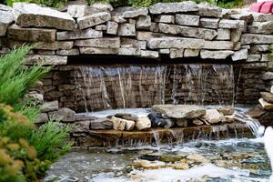 Beautiful garden with stone waterfall and fountain in front of building. photo