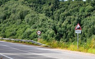 Road signs on a forested highway with speed limit and slope warnings. photo
