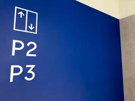 Bright blue wall with clear white markings indicating elevator access to parking levels P2 and P3, ideal for navigation, signage and wayfinding concepts in commercial spaces photo