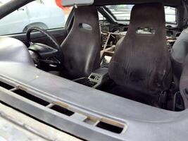Old sport car interior with worn bucket seats, stripped rear section and roll cage installation, showcasing restoration stage before final rebuild and customization photo