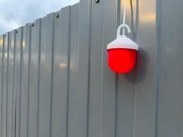 Close up of red warning light mounted on gray metal fence at construction site during twilight. The glowing lamp adds contrast and draws attention to safety and hazard awareness in public spaces photo