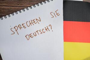 Concept of with question sprechen sie deutsch write on book and flag of germany isolated on Wooden Table. photo