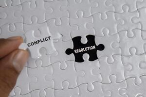 Hand holding piece of jigsaw puzzle with word Conflict resolution. Business and finance concept photo
