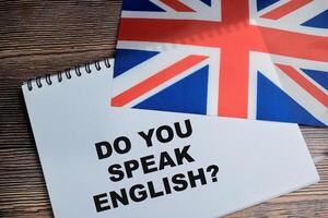 Concept of do you speack english write on book and flag of the united kingdom isolated on Wooden Table. photo