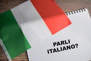 Concept of with question parli italiano write on book and flag of Italy isolated on Wooden Table. photo
