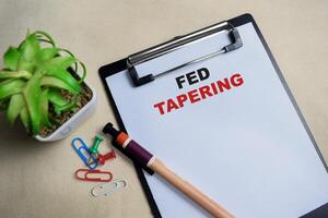 Concept of Fed tapering write on clipboard isolated on Wooden Table. photo