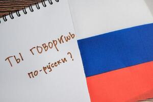 Concept of with question do you speak russian write on book and flag of russia isolated on Wooden Table. photo
