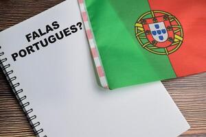 Concept of with question falas portugues write on book and flag of portugal isolated on Wooden Table. photo