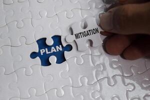 Hand holding piece of jigsaw puzzle with word Mitigation plan. Business and finance concept photo