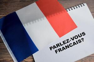 Concept of with question parlez-vous francais write on book and flag of french isolated on Wooden Table. photo