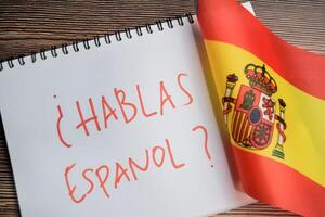 Concept of with question hablas espanol write on book and flag of spain isolated on Wooden Table. photo