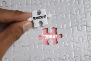 Hand holding piece of jigsaw puzzle with word Permanent temporary. Business and finance concept photo