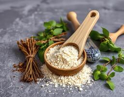 Oat flakes in wooden bowl with wooden scoop and natural herbs on gray surface photo