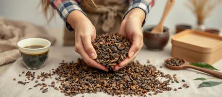 Dried tea leaves held in hands with cup of tea and wooden utensils on table photo
