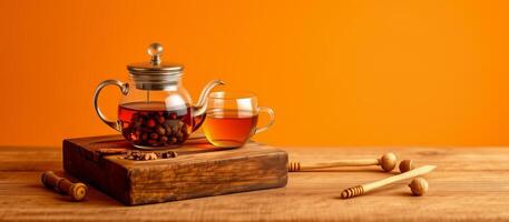 Glass teapot and cup with herbal tea wooden board with honey dippers table, warm orange photo