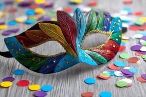 Colorful carnival mask lying on gray wooden table with confetti surrounding it photo