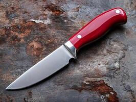Hunting knife with red handle resting on rusty metal surface photo