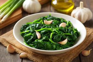 Steamed spinach with garlic cloves and olive oil on rustic wooden table photo